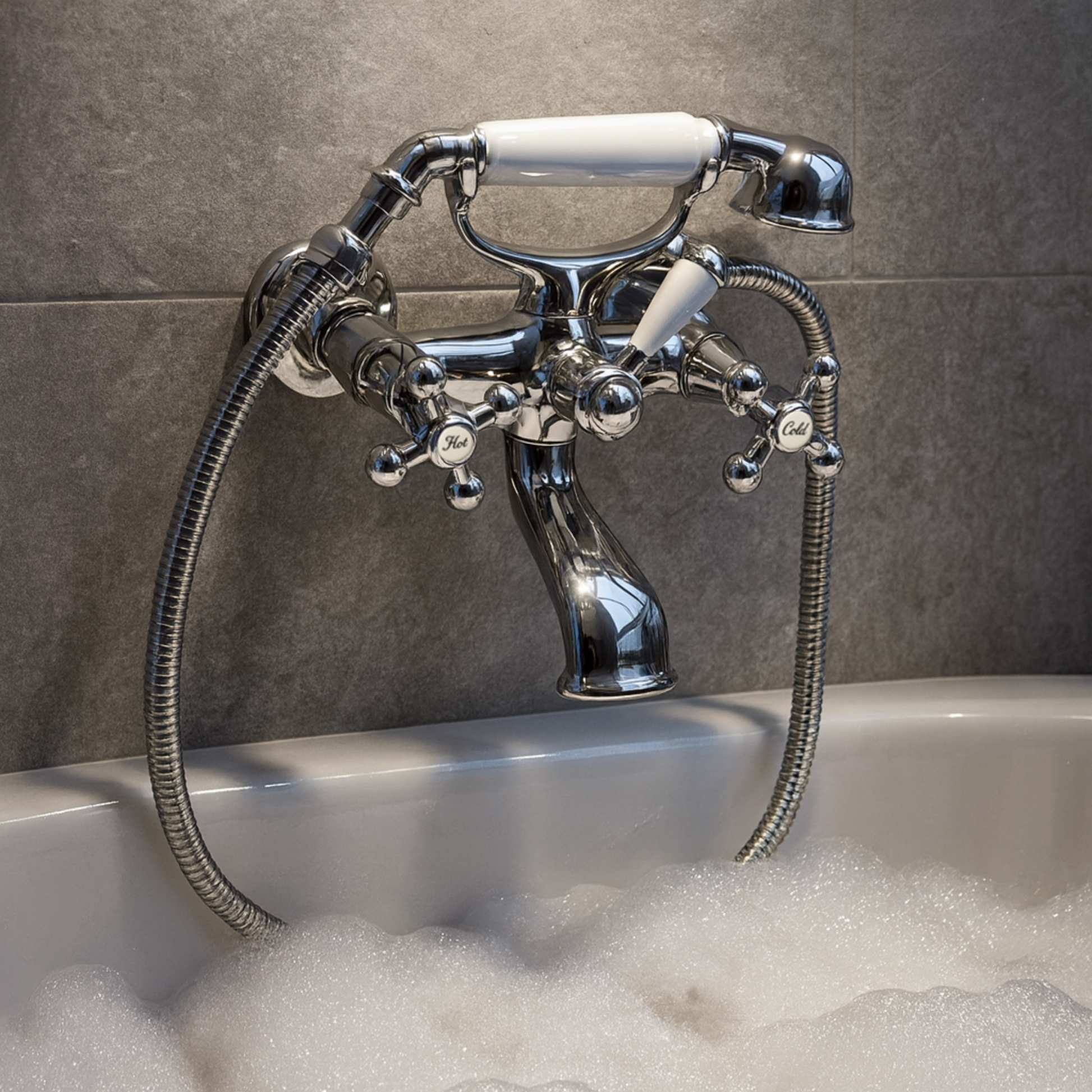 Chrome bathtub faucet with handheld shower head in a tiled bathroom